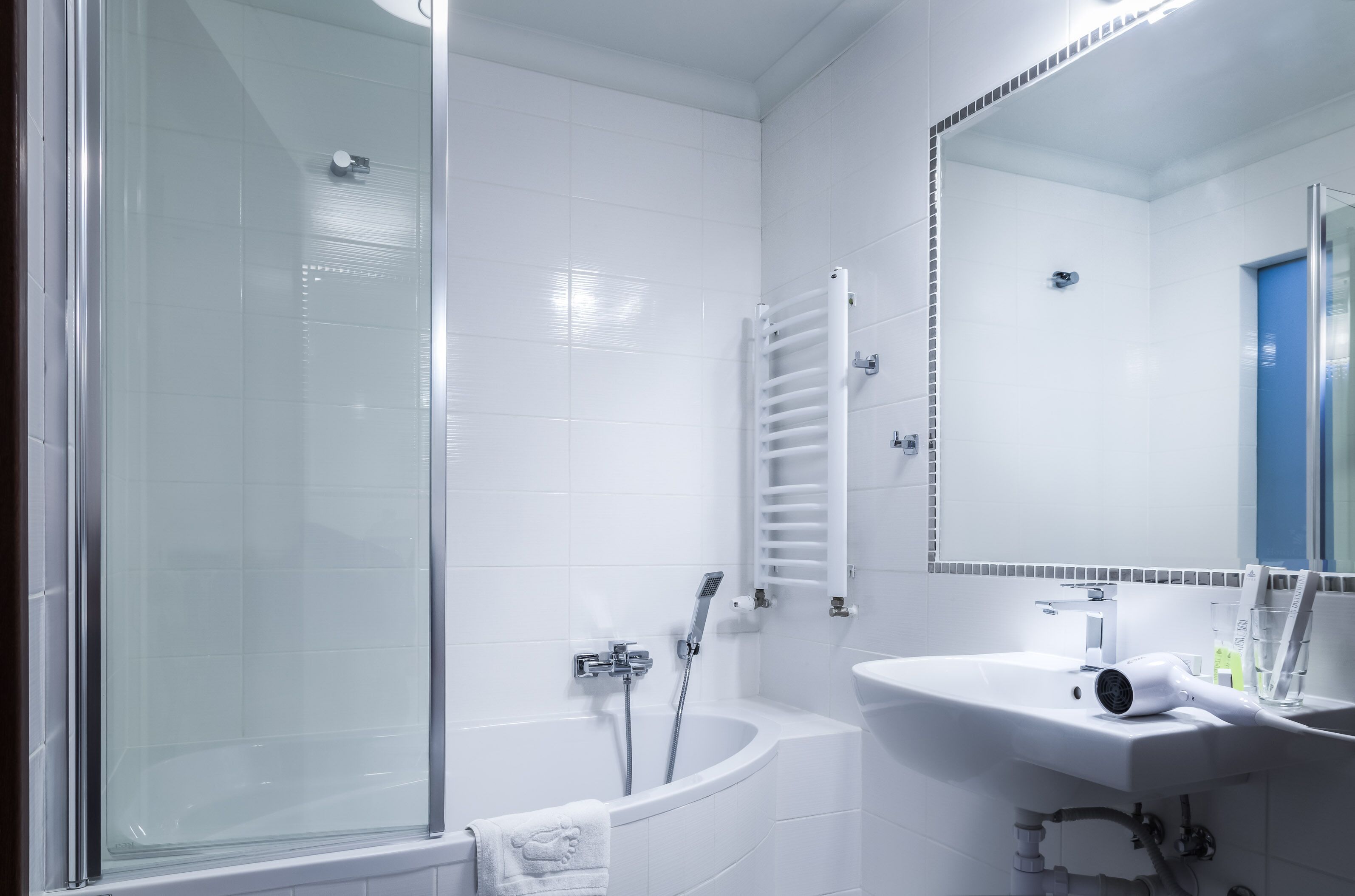 Un baño moderno con ducha de vidrio, bañera blanca y lavamanos con espejo.