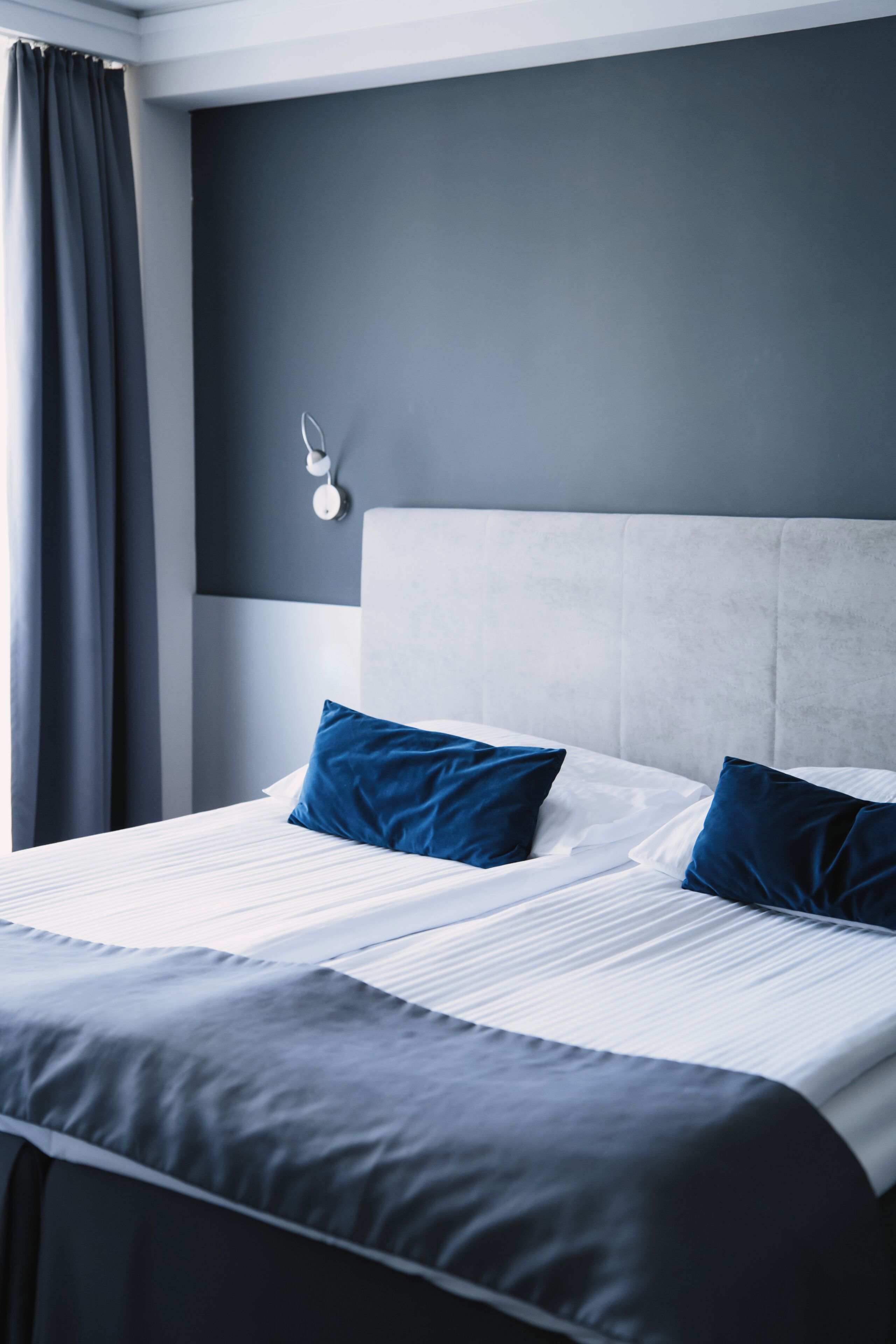 Una habitación de hotel con una cama grande, un cabecero y una ventana con cortinas.