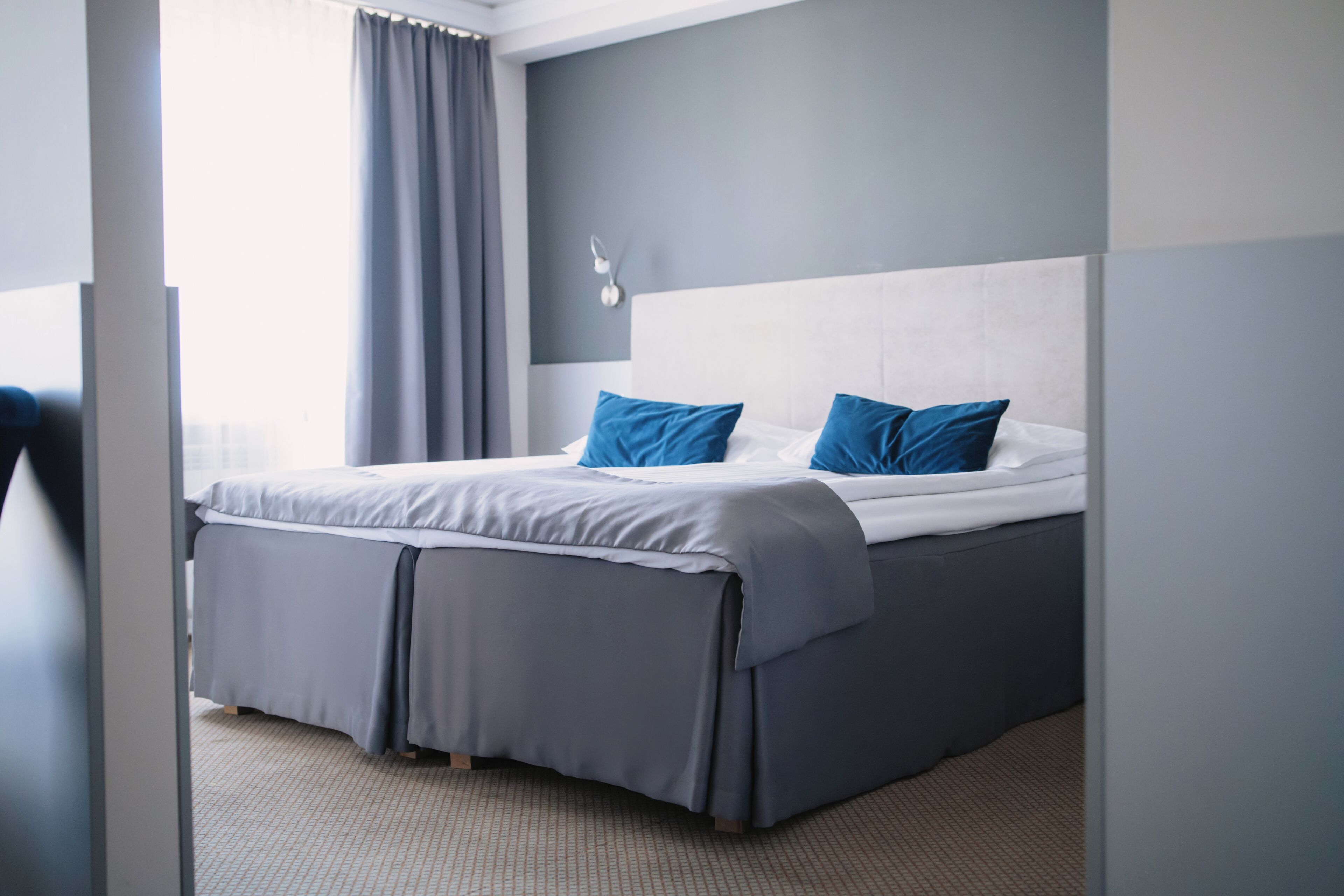 A modern hotel room with a large bed, grey bedding, and a view of the city.