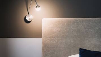 Una cama bien hecha con cabecera, una mesita de noche con cajón y una lámpara de pared.