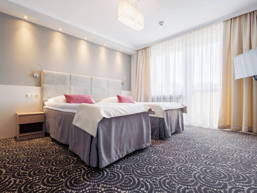 Une chambre d’hôtel avec deux lits, une table de chevet, un téléviseur et une grande fenêtre avec des rideaux.