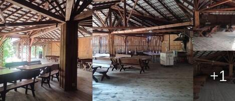 Un intérieur rustique en bois, avec de hauts plafonds et des poutres apparentes, comprenant plusieurs tables et bancs en bois.