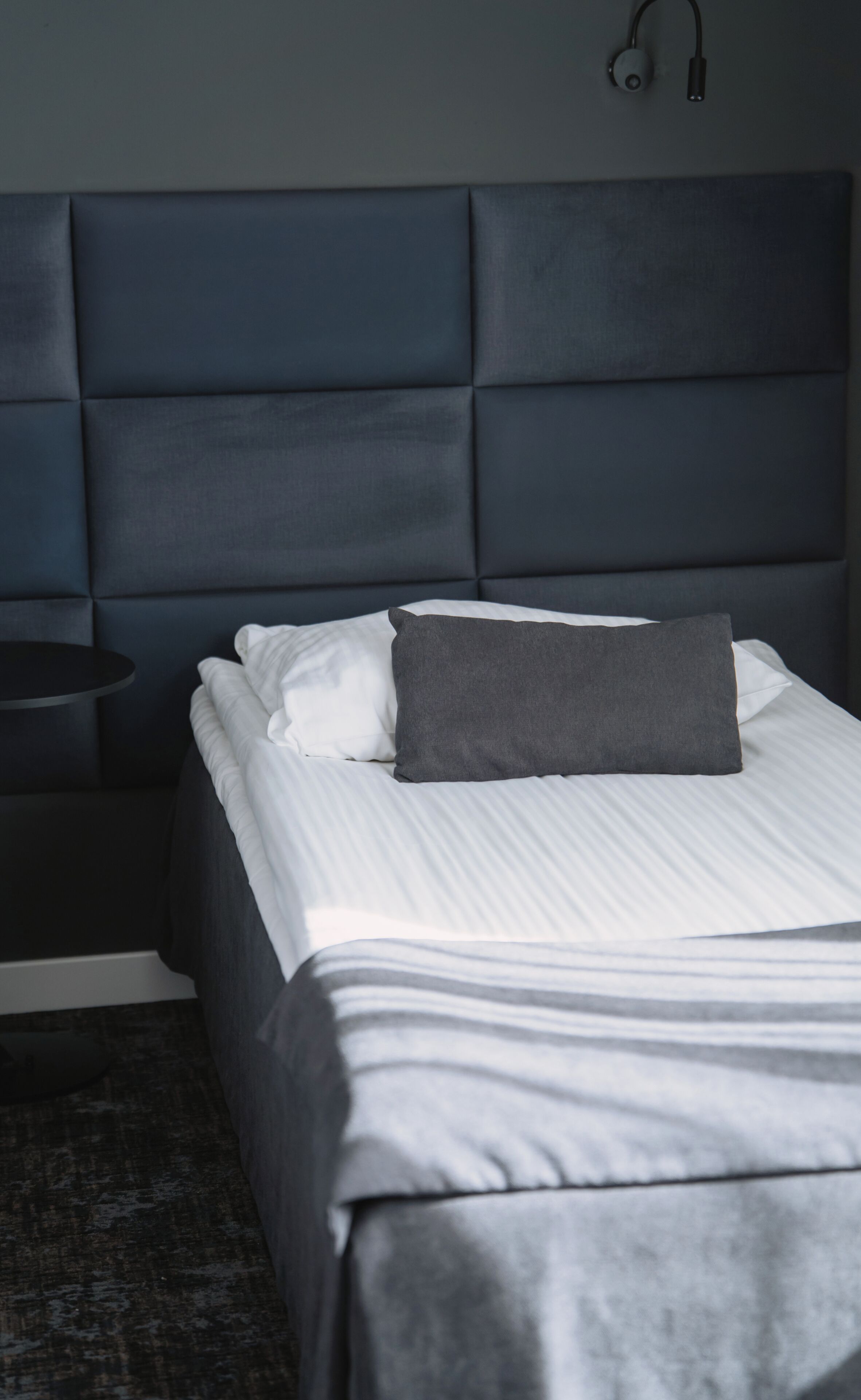 A bed with a headboard, a bedside table, and a wall-mounted light.