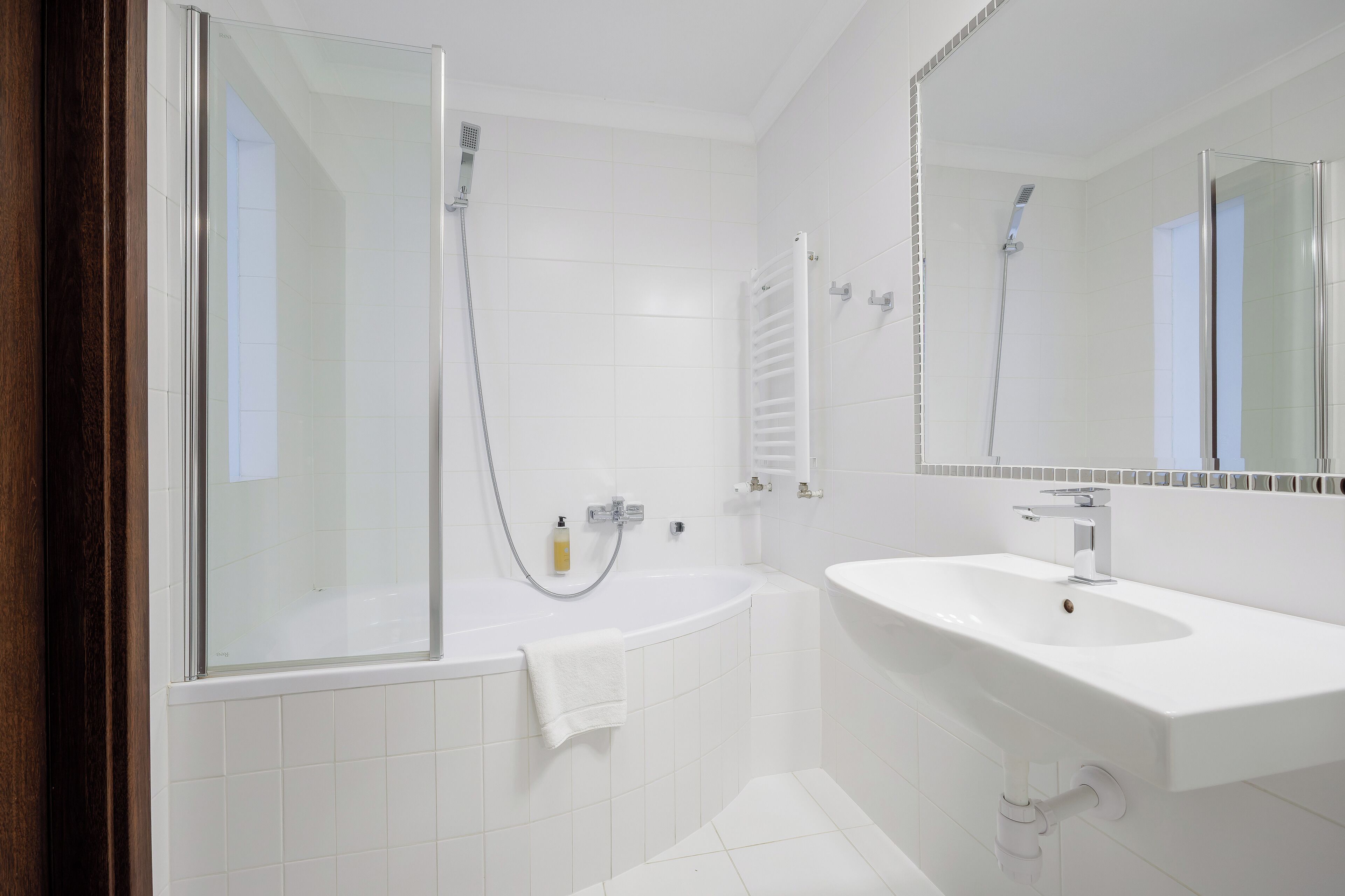 A modern bathroom with a glass-enclosed shower, a white bathtub, and a sink with a mirror above it.