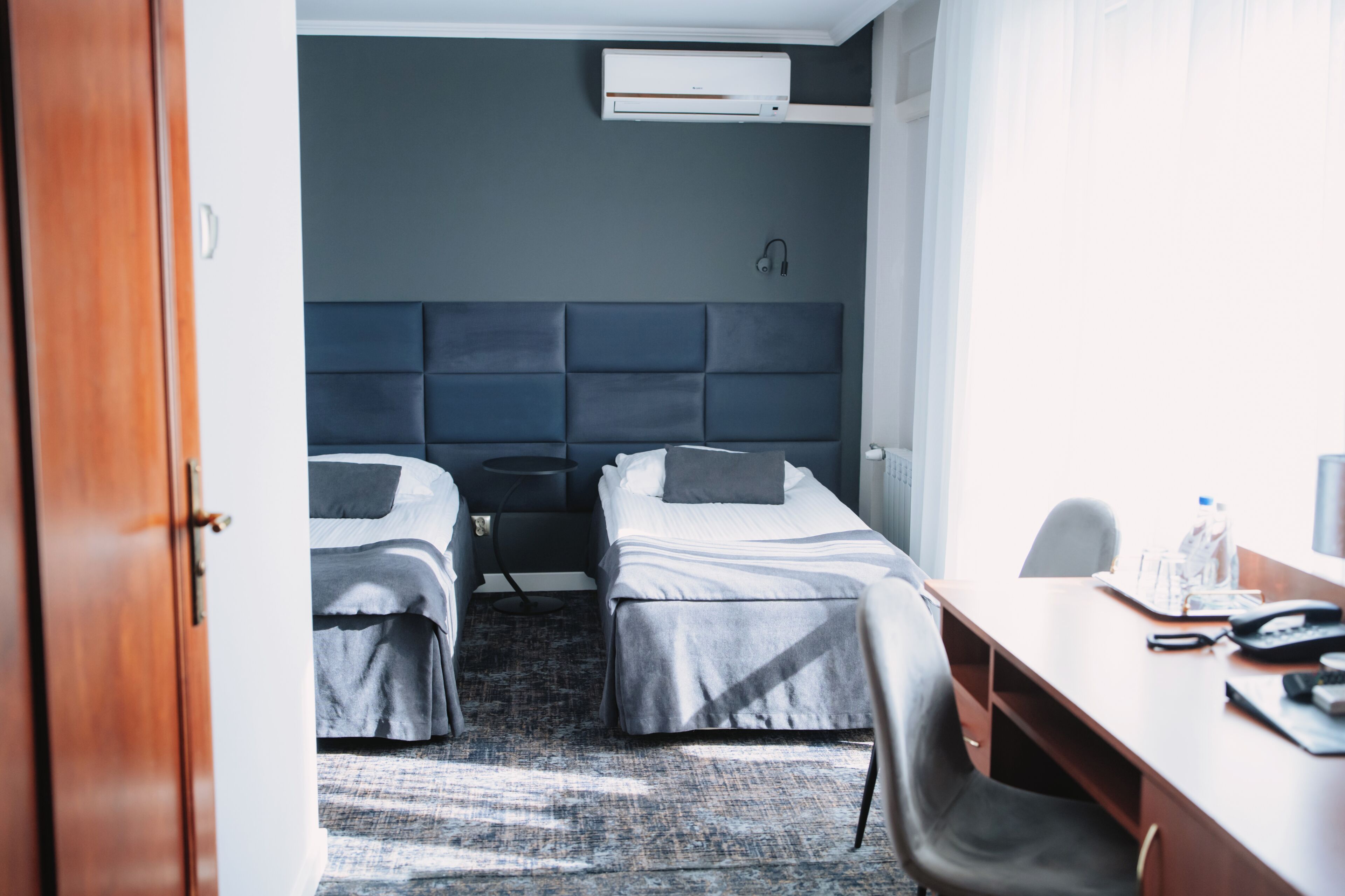 Habitación de hotel con dos camas, un escritorio, una silla, una botella de agua, un teléfono y un equipo de aire acondicionado.