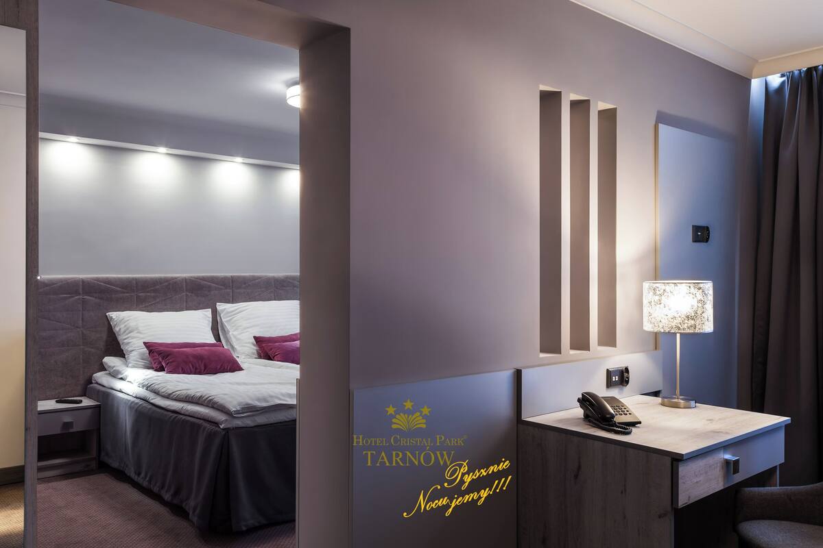 Una habitación de hotel con cama, mesita de noche, lámpara y escritorio con teléfono.