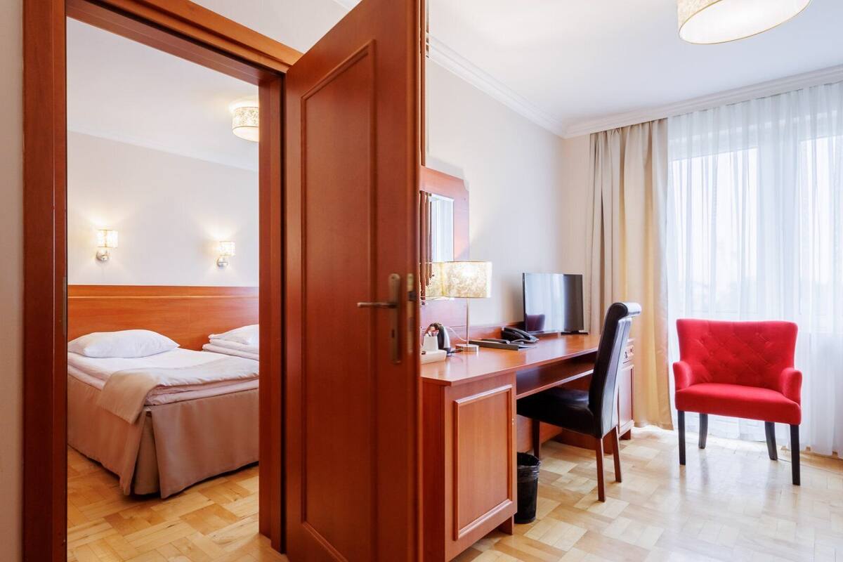 Habitación de hotel con cama, escritorio, silla, televisor y ventana con cortinas.