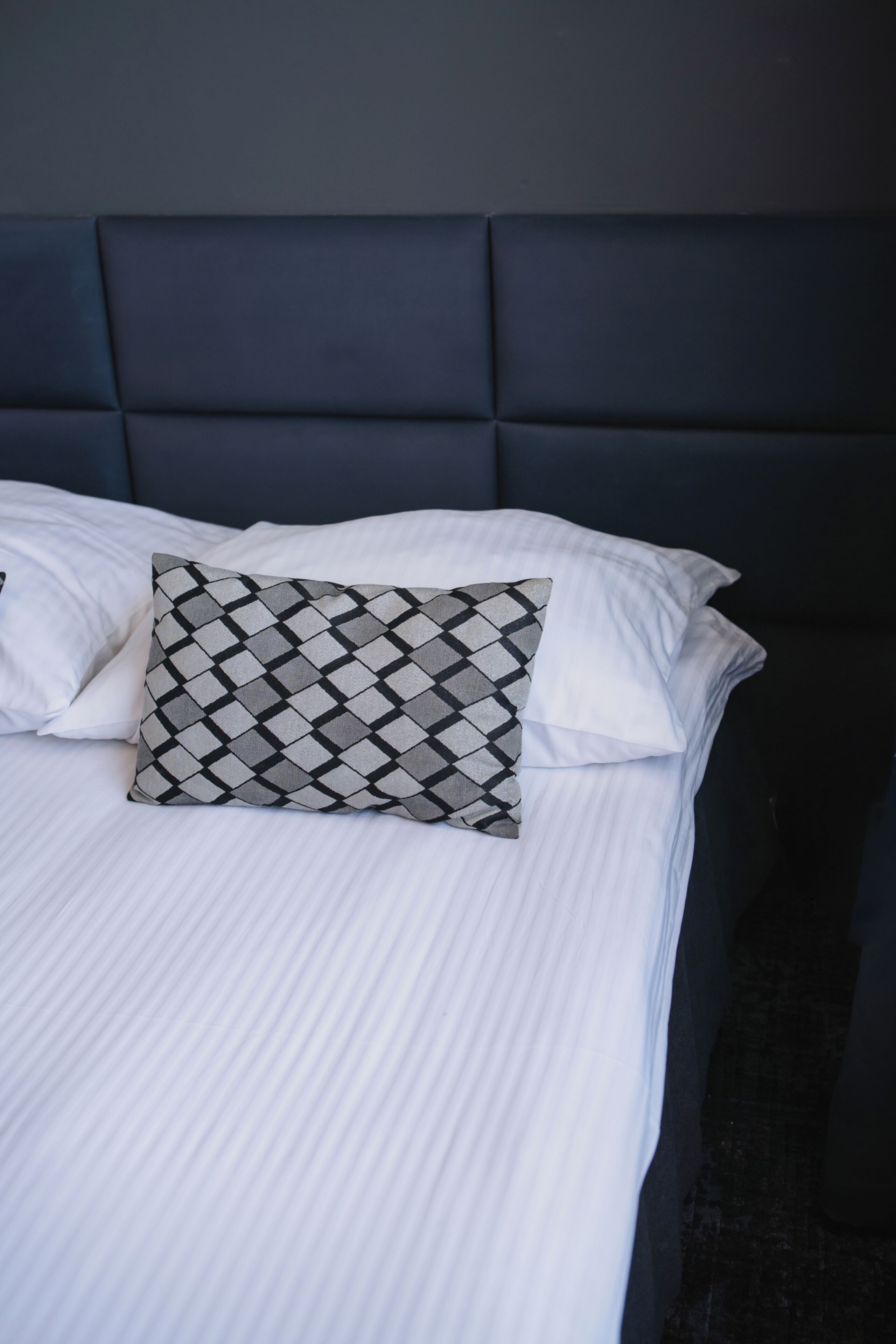 Un lit avec un oreiller à motifs, une literie blanche et une tête de lit sombre.