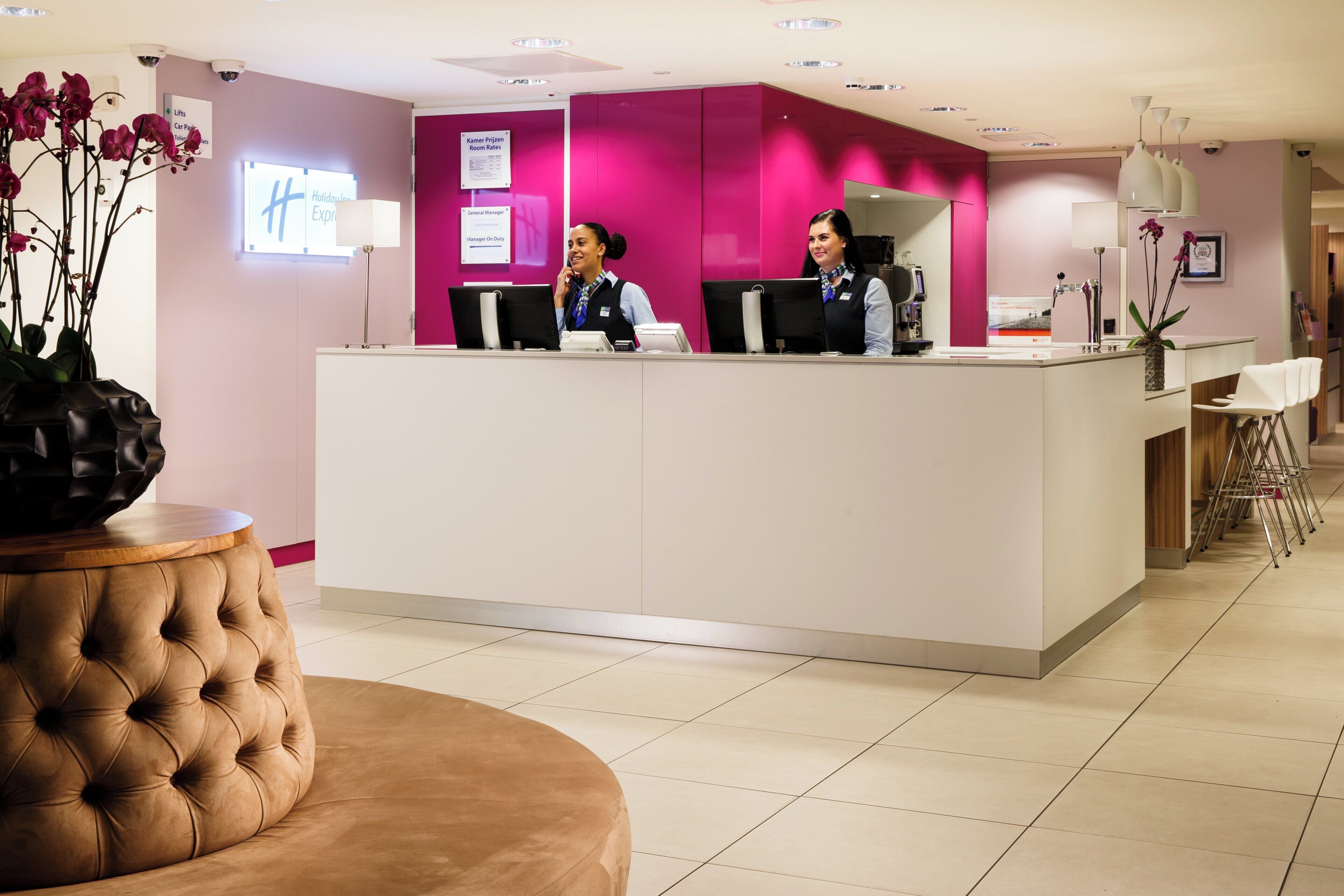 Eine Hotelrezeption mit zwei Mitarbeitern, einem bequemen braunen Sofa und einer Orchideen-Vase.