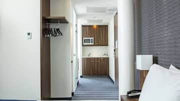 Een hotelkamer met een bed, een nachtkastje met een lamp, een kleine kitchenette met een magnetron en een badkamer door een geopende deur zichtbaar.