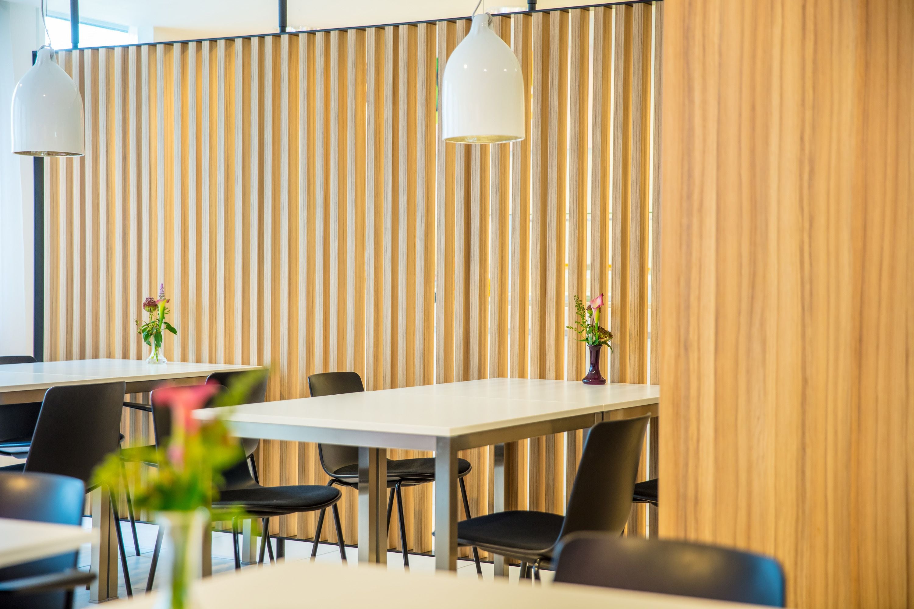 A modern dining area with striped wooden partitions, white tables, and black chairs.