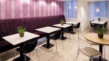 Een modern interieur met een paarse bank, witte tafels en zwarte stoelen, waarvan sommige met planten.