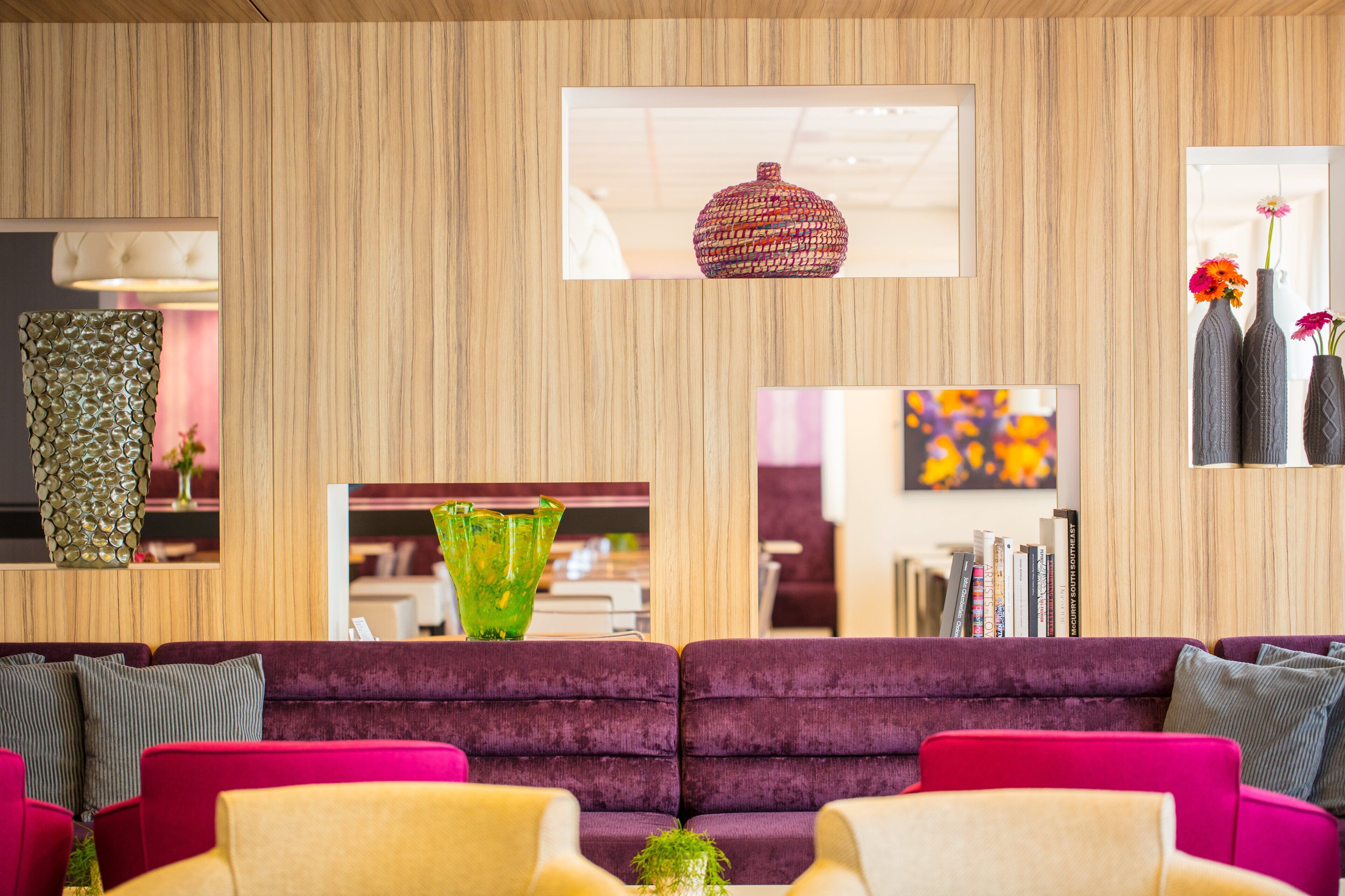 Een moderne woonkamer met een houten wand, een paarse bank, een groene vaas en een rode geweven mand.