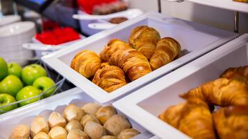 A buffet with various food items including croissants, pastries, and green apples.
