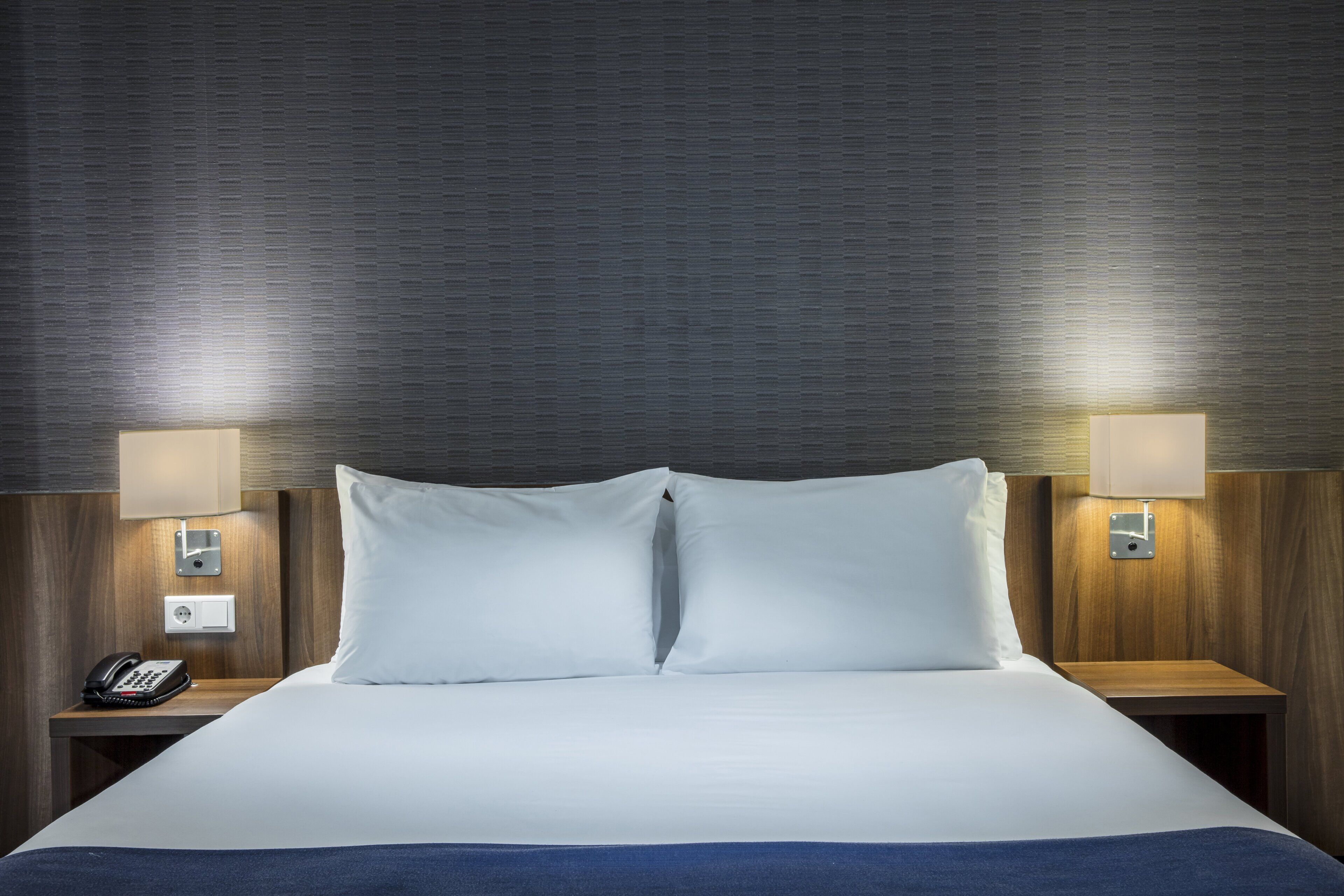 Een hotelkamer met een groot bed, twee nachtkastjes, een telefoon en wandlampen.