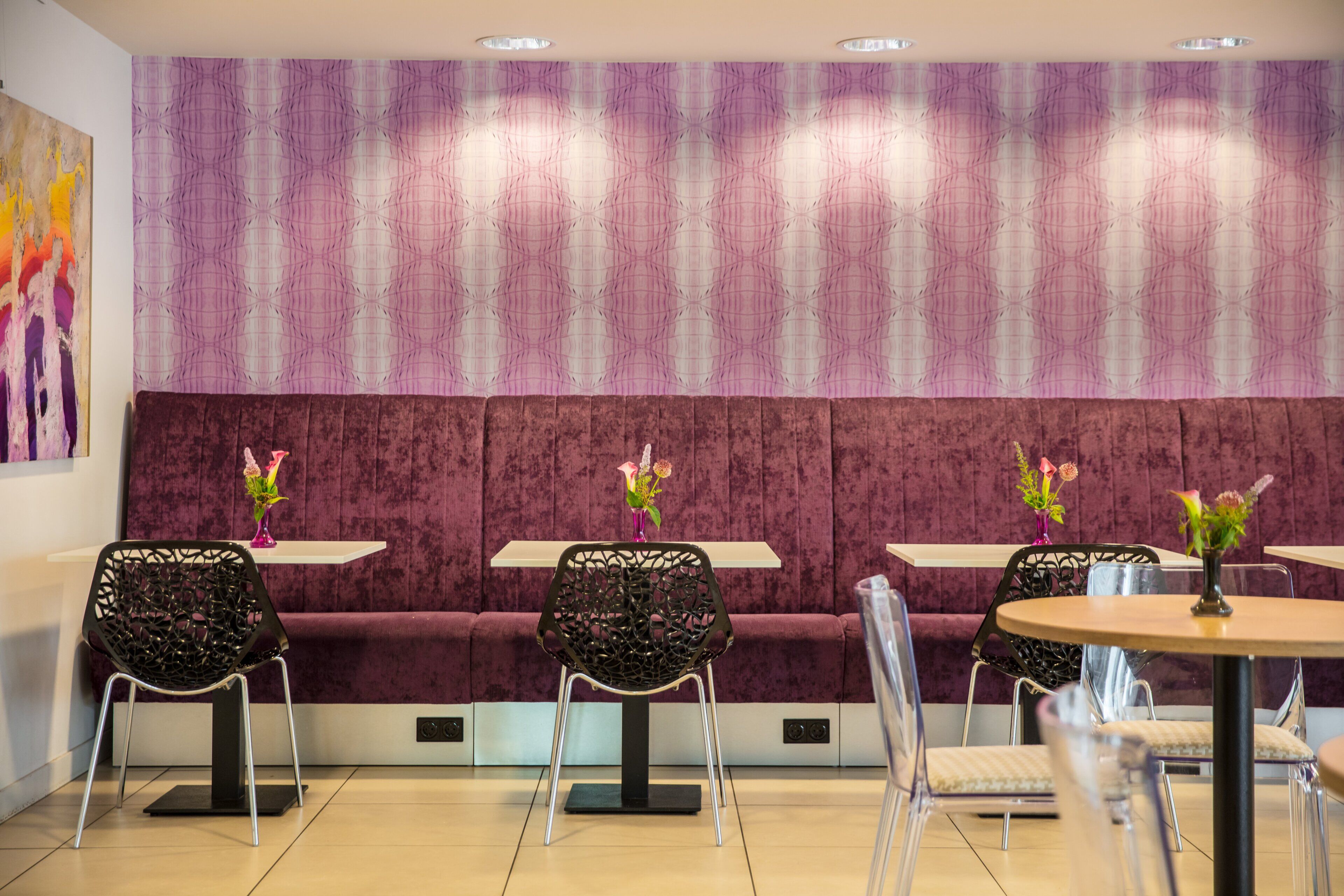 Un interior moderno con un banco tapizado de púrpura, sillas traslúcidas y una mesa redonda con un jarrón de flores.