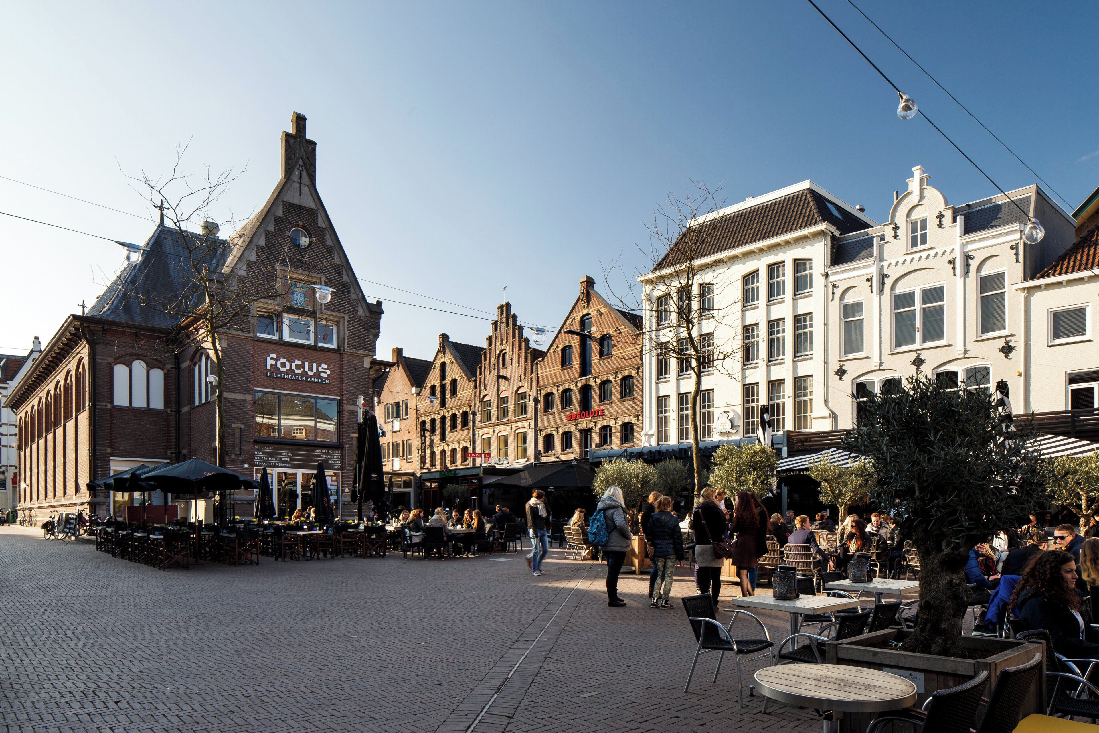 Una plaza histórica con arquitectura europea tradicional, mesas al aire libre para cafés y un cielo despejado.