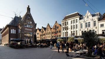 Una plaza histórica con arquitectura europea tradicional, mesas al aire libre para cafés y un cielo despejado.