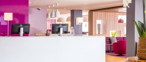 Una zona de recepción moderna con un mostrador blanco, dos monitores y una pared de color rosa intenso.
