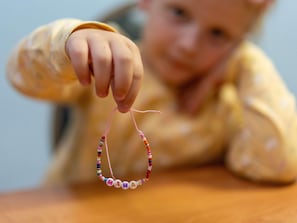 Et barn holder et armbånd med perler, hvor ordet 'MAMA' er stavet.