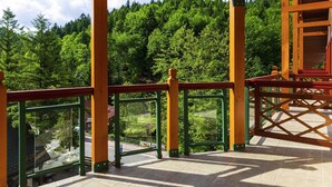Ein überdachter Außenbereich mit Blick auf einen bewaldeten Hang, einem Kachelboden und einem Geländer.