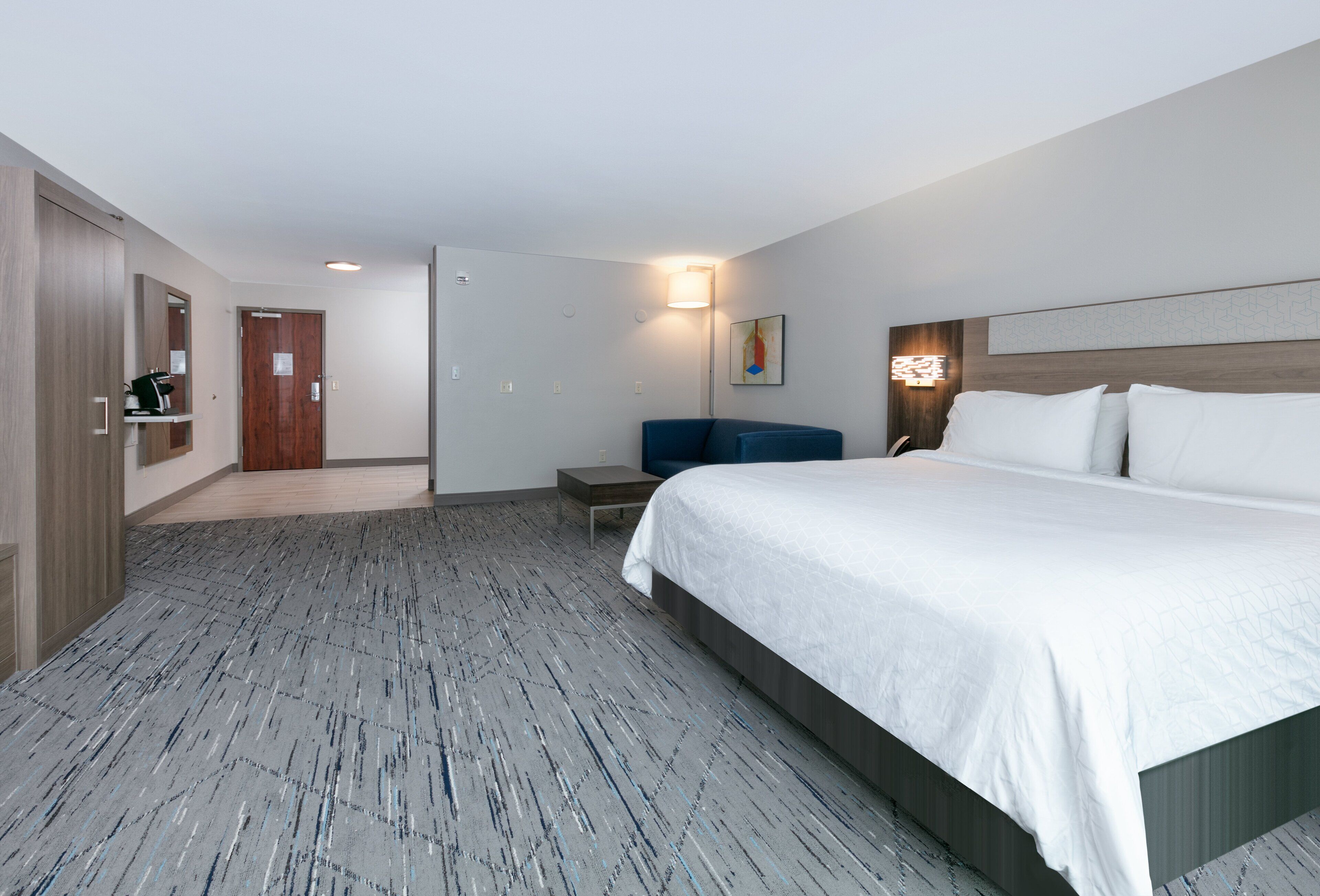 Habitación de hotel con una cama grande, un escritorio, una silla, un armario y una mesita.