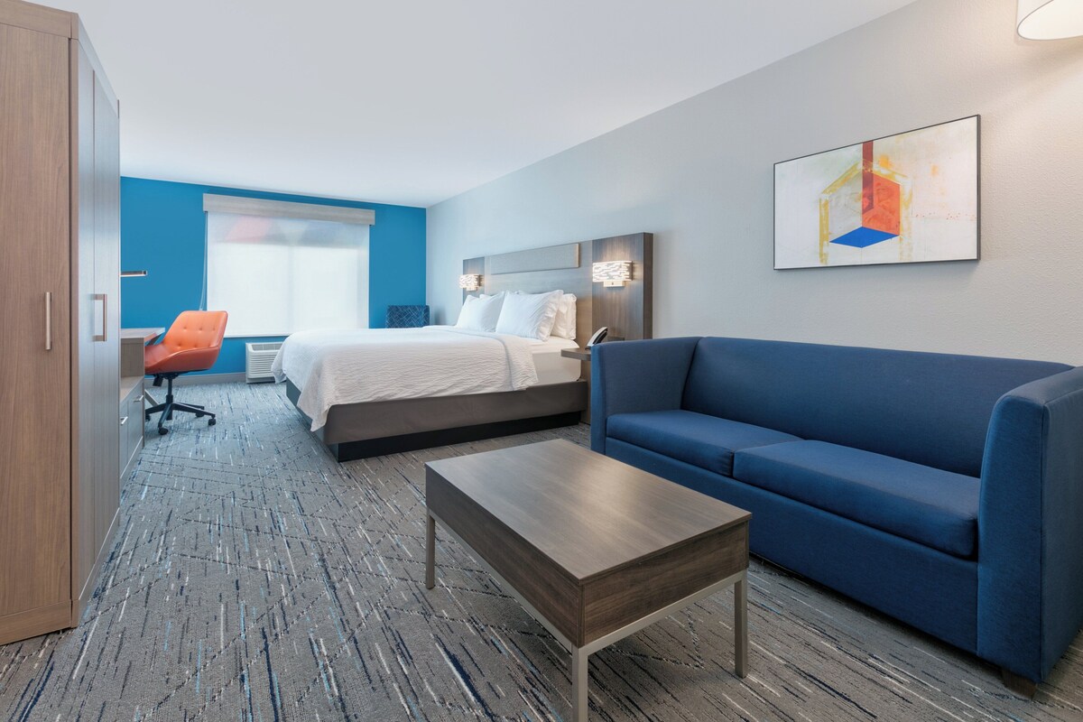 Een hotelkamer met een bed, een blauwe bank, een houten salontafel en een bureau met een oranje stoel.