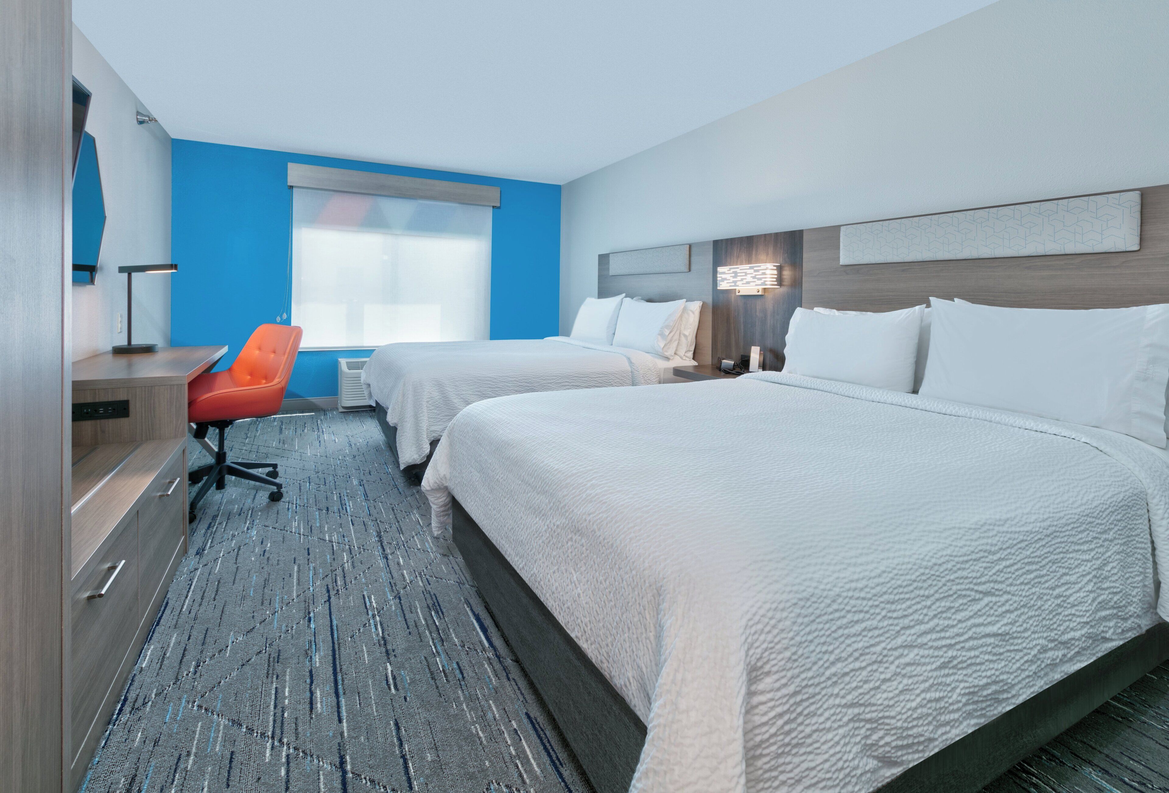 A hotel room with two beds, a desk with a chair, a large window, and a modern wall design.