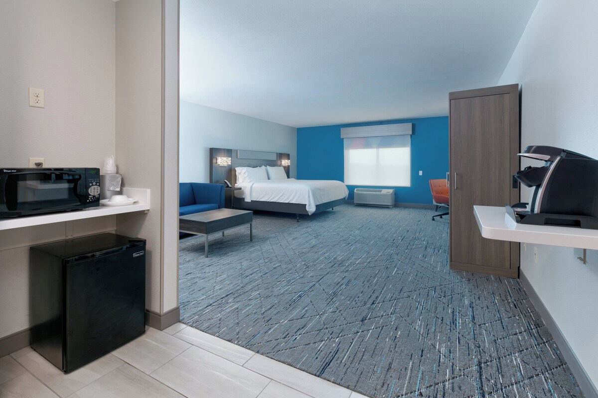 Een hotelkamer met een bed, een bureau, een magnetron en een prullenbak.