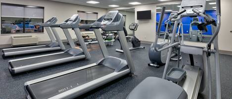 A gym with treadmills, elliptical machines, and a mirrored wall.