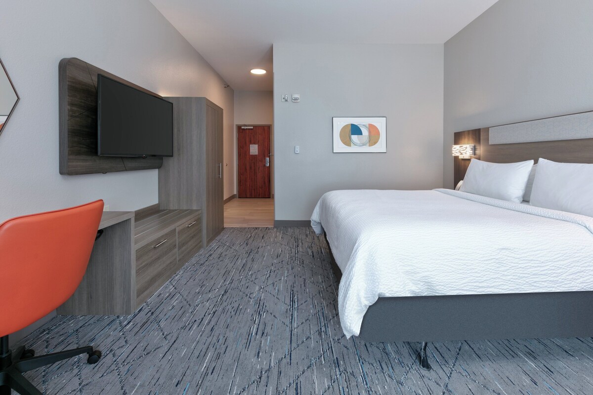 Hotelkamer met een bed, een bureau met stoel, een aan de muur bevestigde televisie en een deur naar een andere kamer.