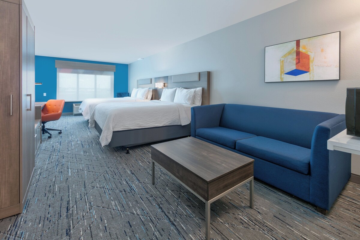 Een hotelkamer met een bed, een blauwe bank, een houten salontafel en een bureau met een oranje stoel.