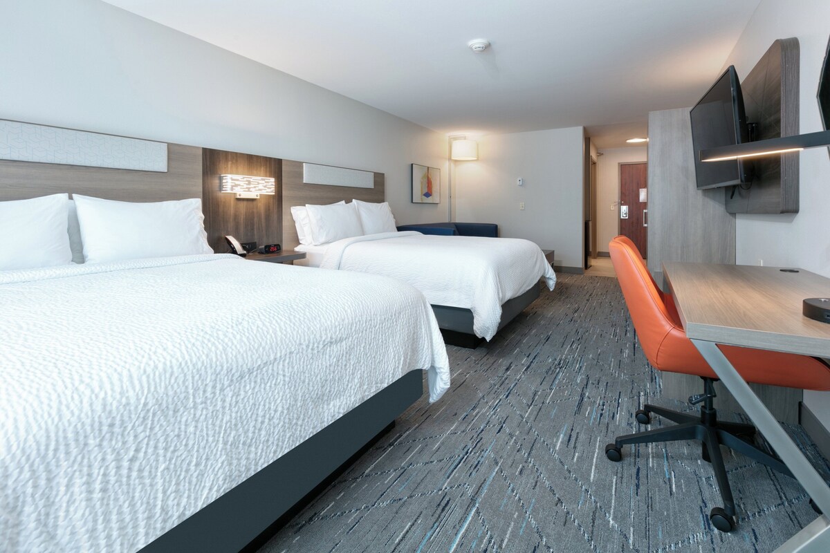 Een hotelkamer met twee bedden, een bureau, een stoel, een flatscreen-televisie en een wandlamp.
