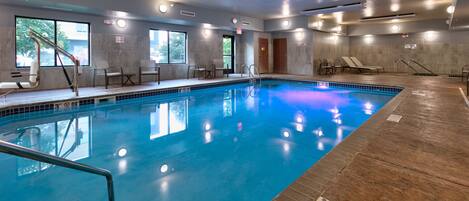 Una piscina interior con carriles claramente marcados, una silla de salvavidas y una zona junto a la piscina con sillones de descanso.
