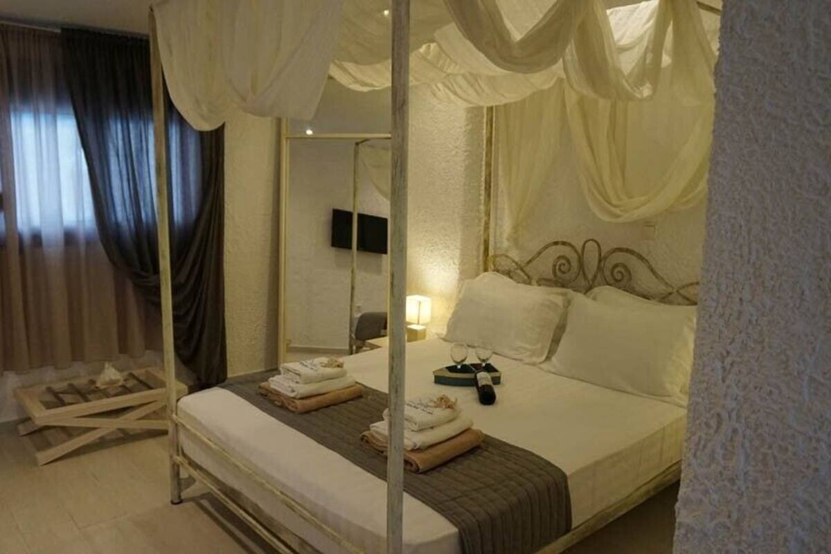 A four-poster canopy bed with a headboard, a bedside table with a lamp, and a mirror on the wall.