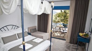 A bedroom with a four-poster bed, a sofa, a small table with fruit, and a balcony with a table and chairs. - Ariadni Blue Hotel (Sithonia)