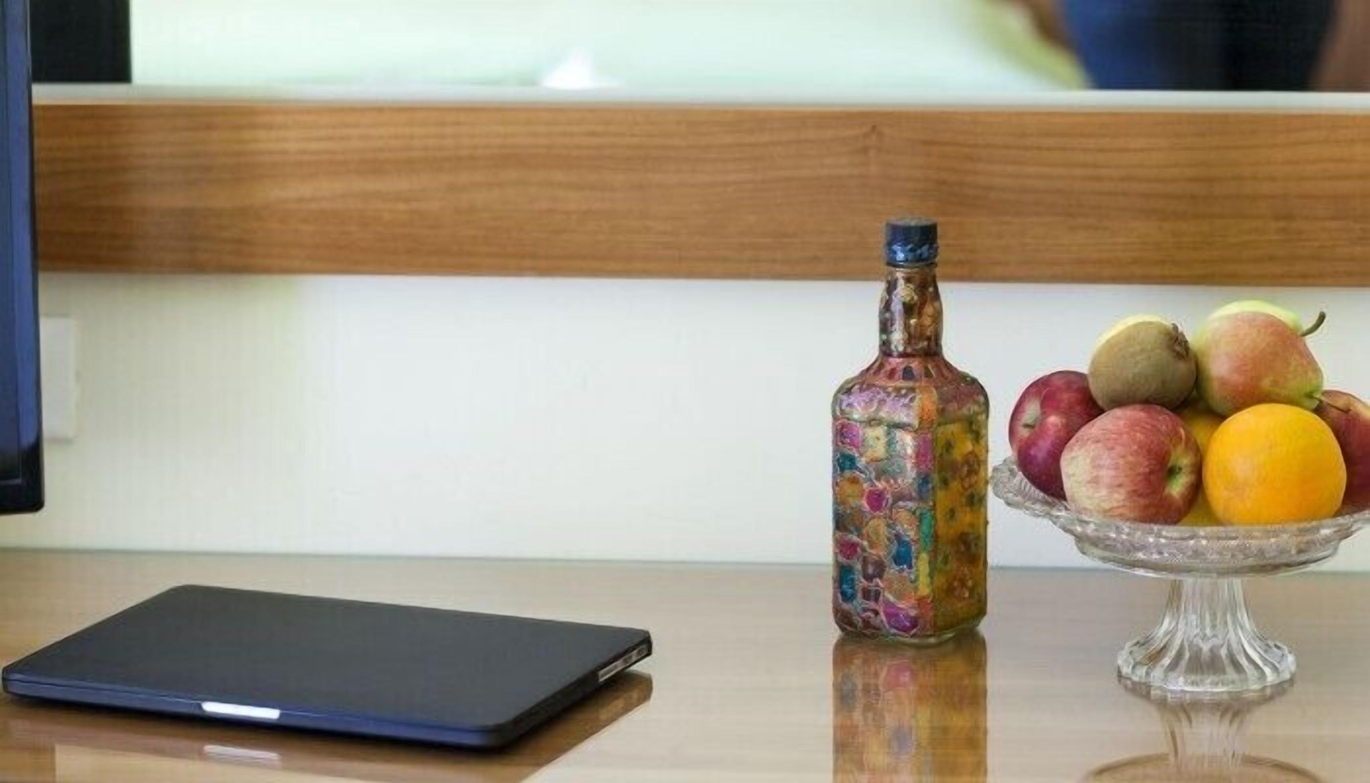 Ein Laptop auf einem Holztisch, eine farbige Flasche und eine Obstschale mit Äpfeln und Birnen.