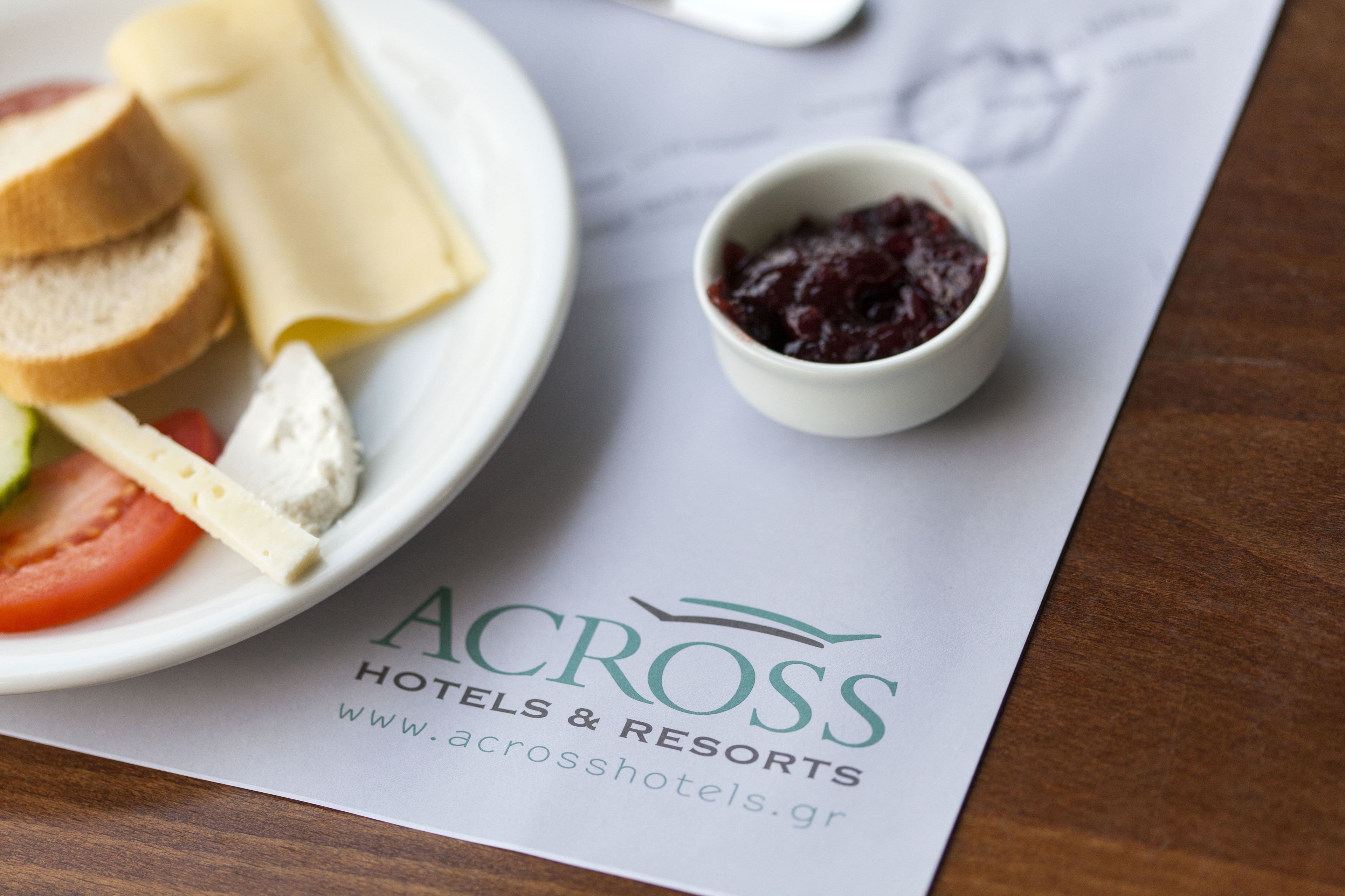 Een bord eten met brood, kaas en tomaat, plus een klein schaaltje jam, op een menu van Across Hotels & Resorts.