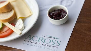 Een bord eten met brood, kaas en tomaat, plus een klein schaaltje jam, op een menu van Across Hotels & Resorts.
