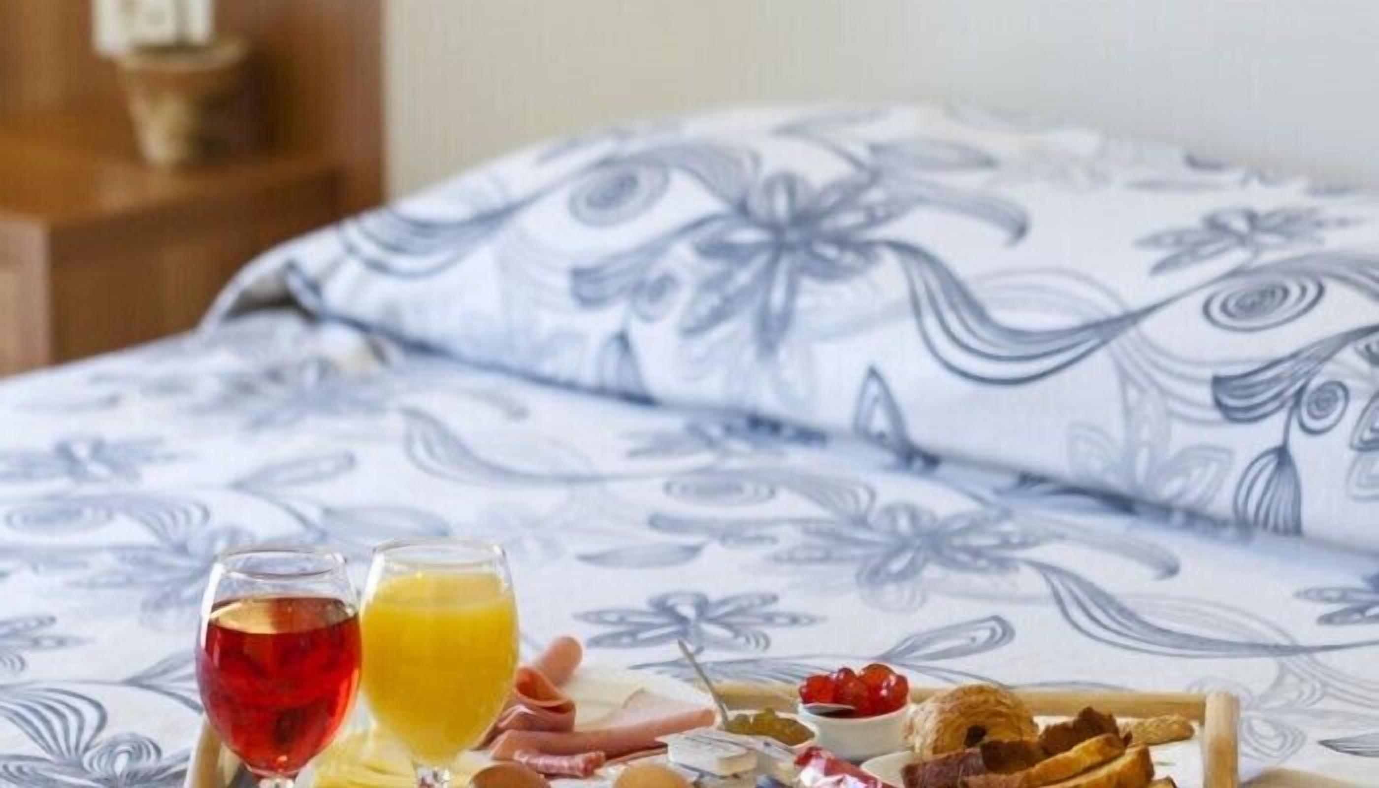 A bed with a floral bedspread, a breakfast tray with croissants, cheese, and jam, and two glasses of juice.
