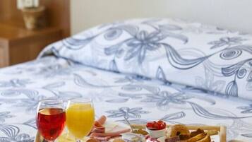 Un lit recouvert d’une couvre-lit à motifs floraux, un plateau de petit-déjeuner avec des croissants, du fromage et de la confiture, et deux verres de jus de fruits.