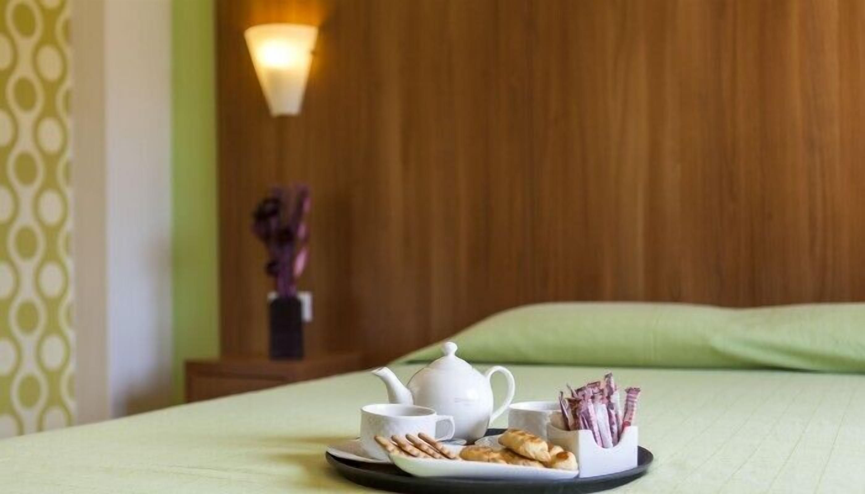 A neatly arranged breakfast tray on a bed with a teapot, cups, and pastries.