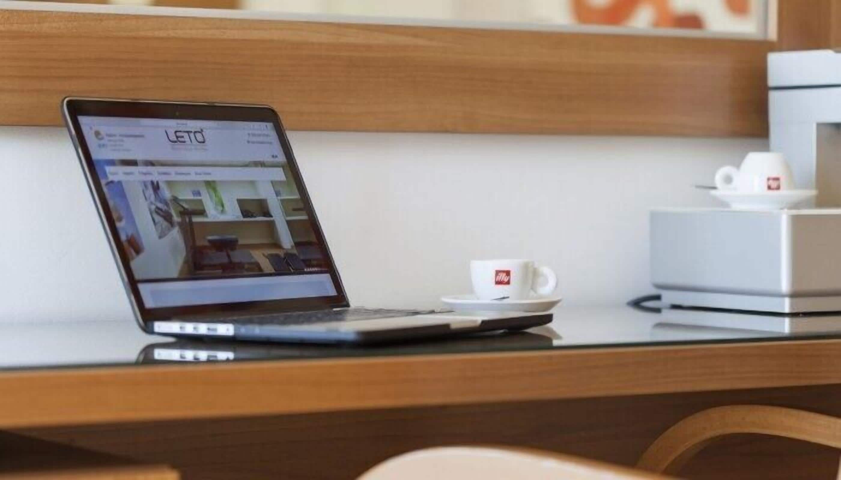 A laptop on a wooden desk with a white cup and saucer beside it.