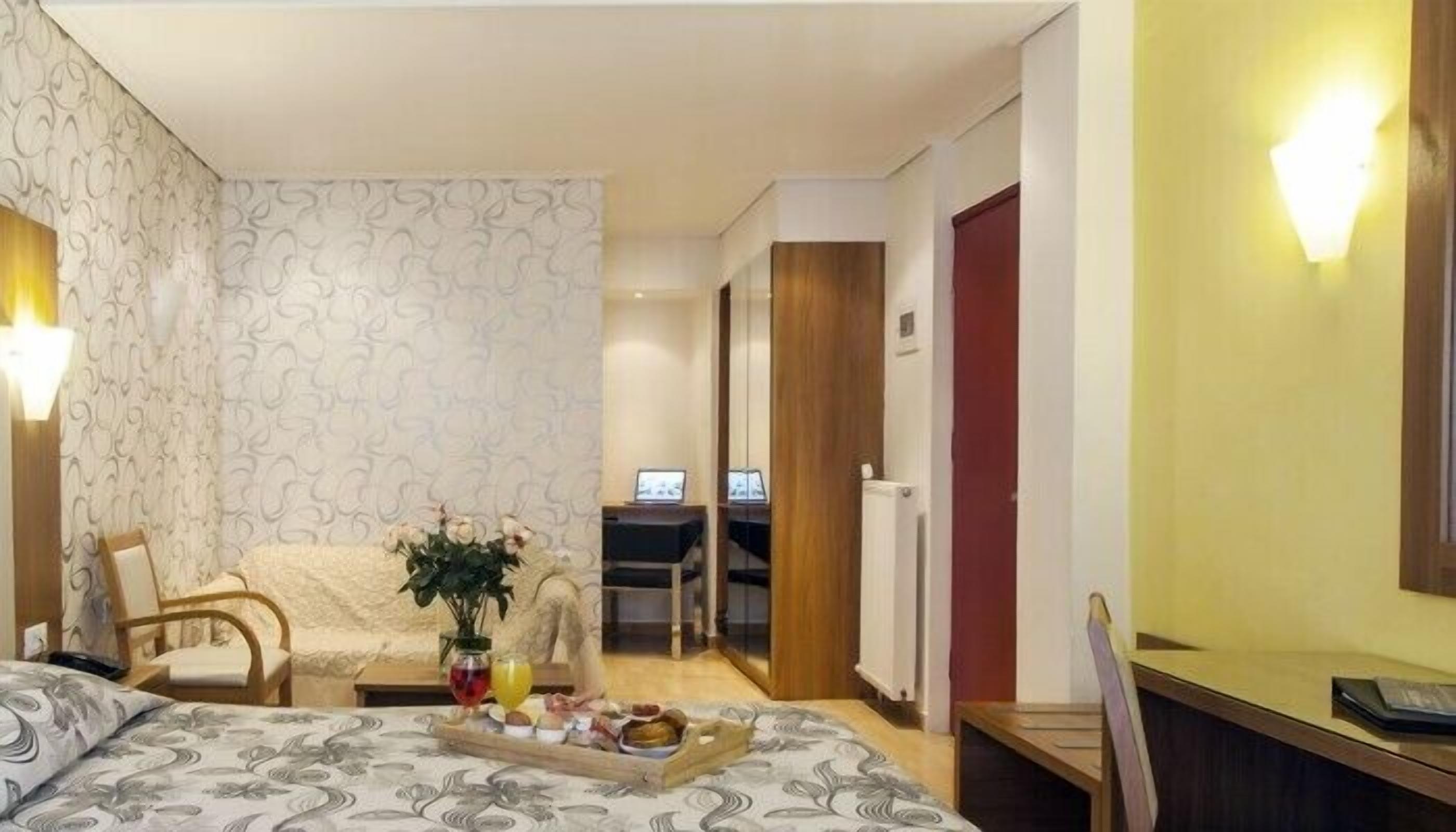 Una habitación de hotel con cama, escritorio, silla, una mesita con una bandeja de comida, una planta y televisor.