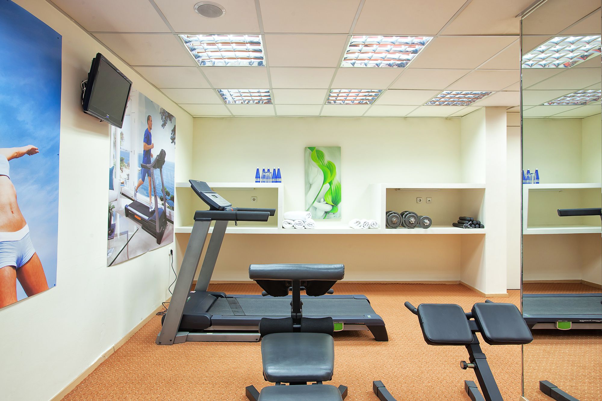 Uma academia com esteiras, bancos de musculação e um painel de espelhos.