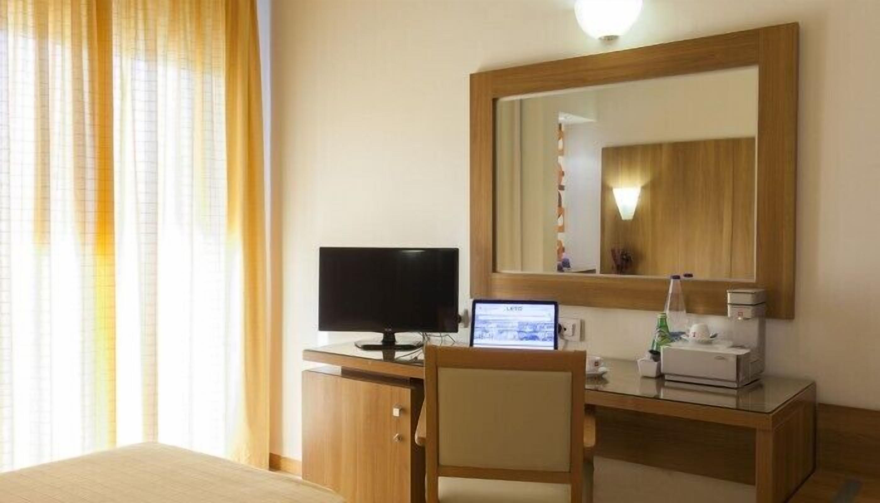 A hotel room with a bed, a desk with a computer, a television, and a mirror.