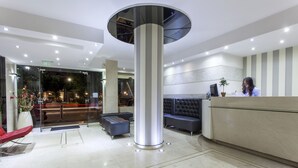 A modern hotel lobby with a central column, seating area, reception desk, and a glass entrance. - Leto Boutique Hotel (Agrinio)