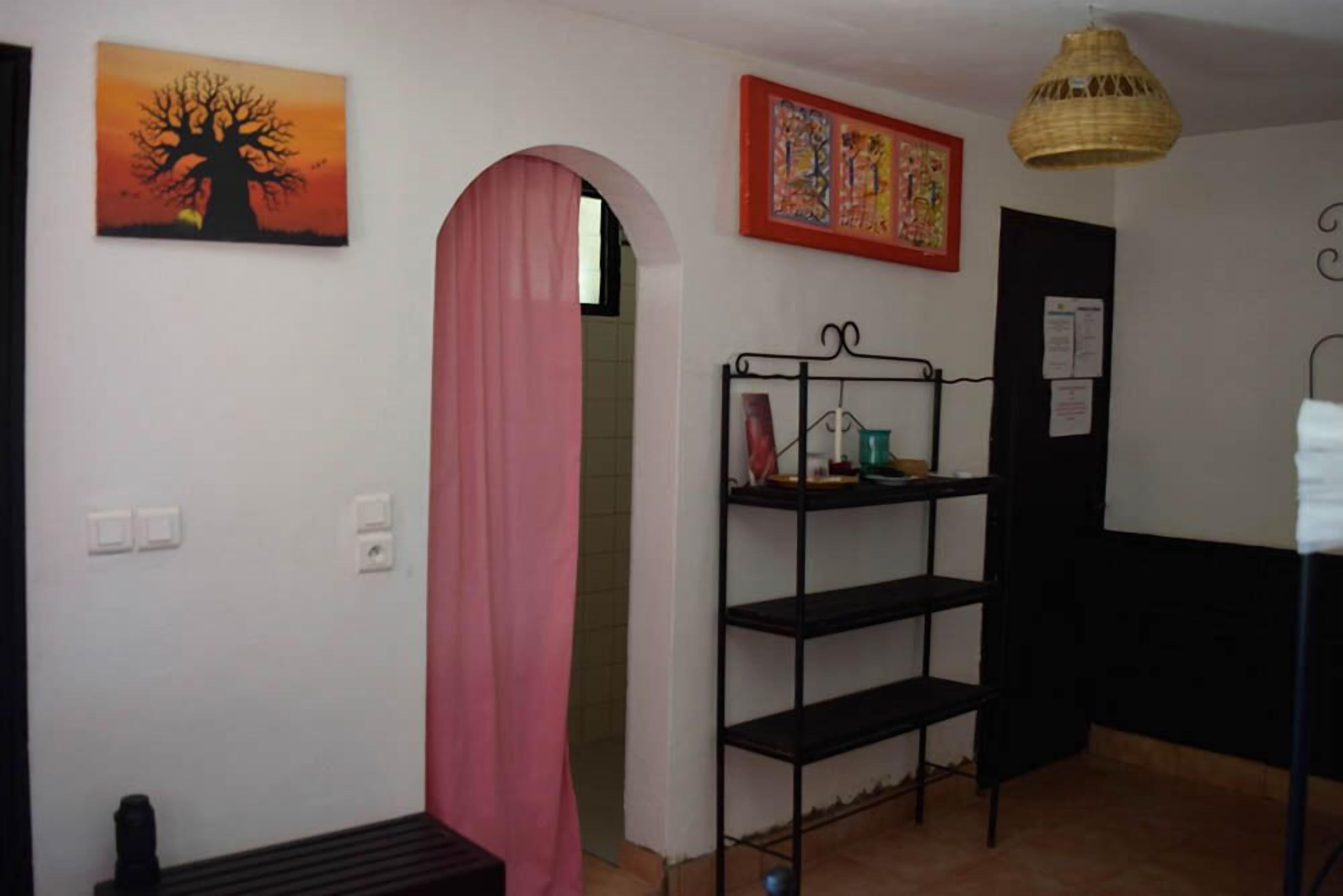 A room with a metal shelf unit, a pink curtain, and a painting of a tree.