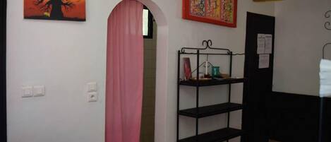 A room with a metal shelf unit, a pink curtain, and a painting of a tree.