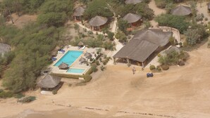 Vista aérea de un resort con piscina, cabañas de techo de paja y una zona de playa.